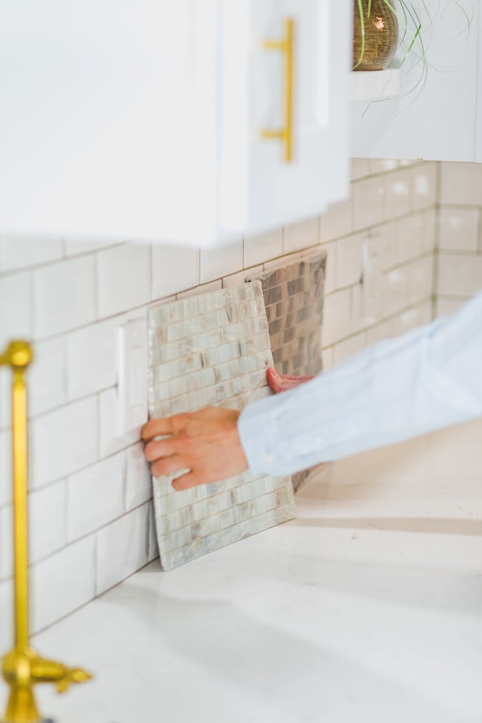 brand-01 Person installing tile backsplash in a bright, modern kitchen setting.